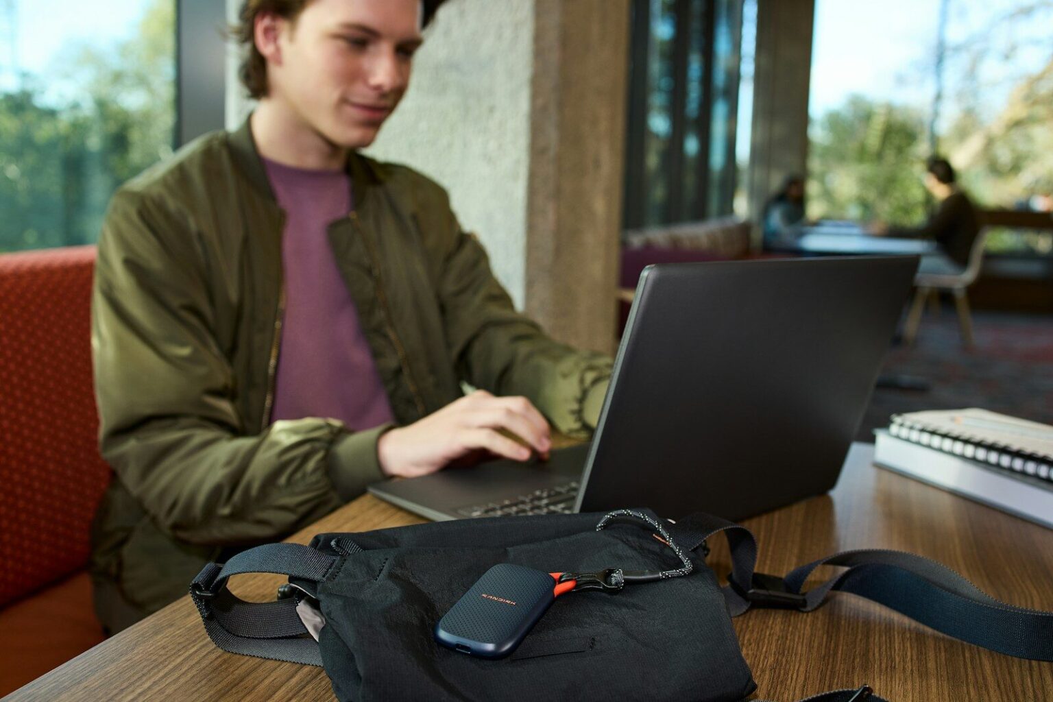 Young man uses laptop, portable storage device on table.